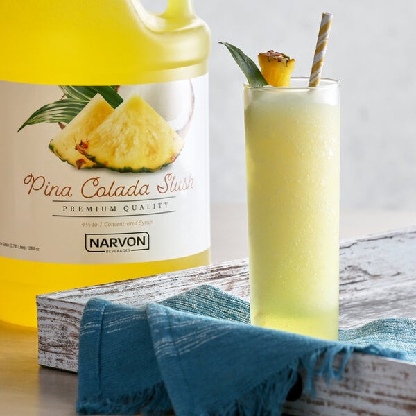 A bottle of Narvon Pina Colada slushy syrup next to a glass of yellow liquid.