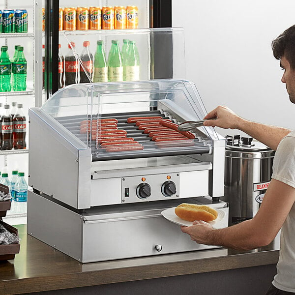 A man using an Avantco slanted hot dog roller to cook hot dogs.