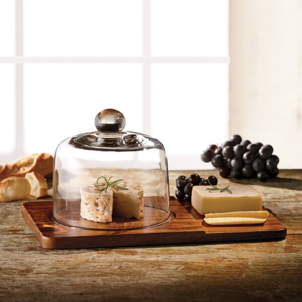 An American Atelier wood cheese board with glass dome cover on a table with cheese and grapes.