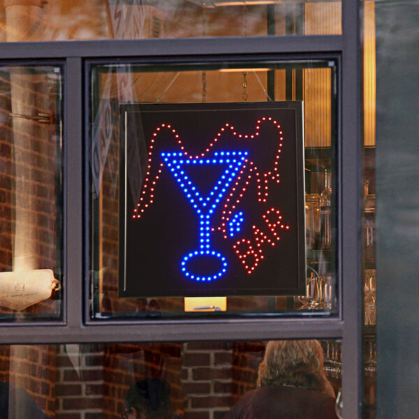 A LED square bar sign that says "drink" in blue and red displayed in a window.
