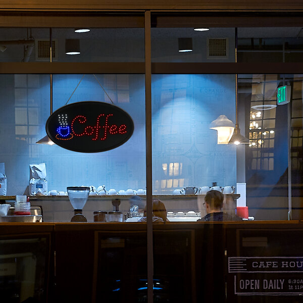 An oval LED coffee sign in a window of a coffee shop.