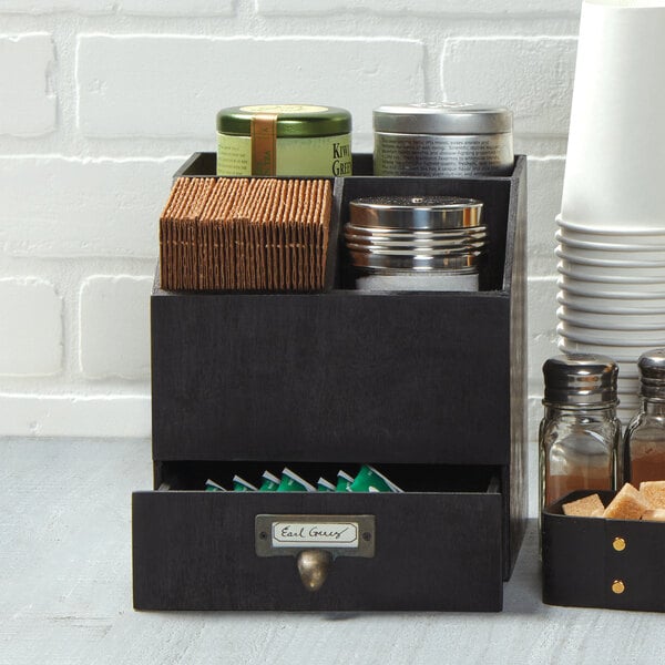 An American Metalcraft black poplar wood coffee caddy on a counter with condiments and sugar containers in it.