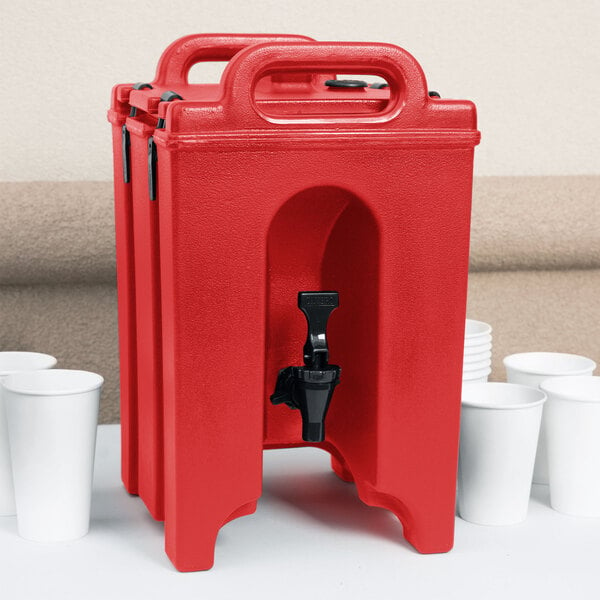 A red Cambro insulated beverage dispenser with a black spigot on a white table with white cups.