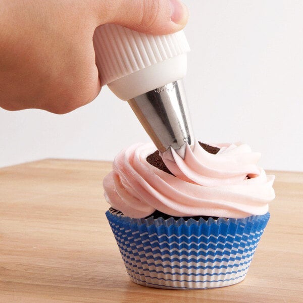 A hand using an Ateco closed star piping tip to frost a cupcake.