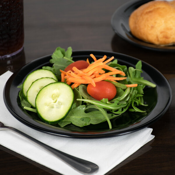 A close up of a Carlisle black melamine plate with salad, cucumbers, carrots, and tomatoes.