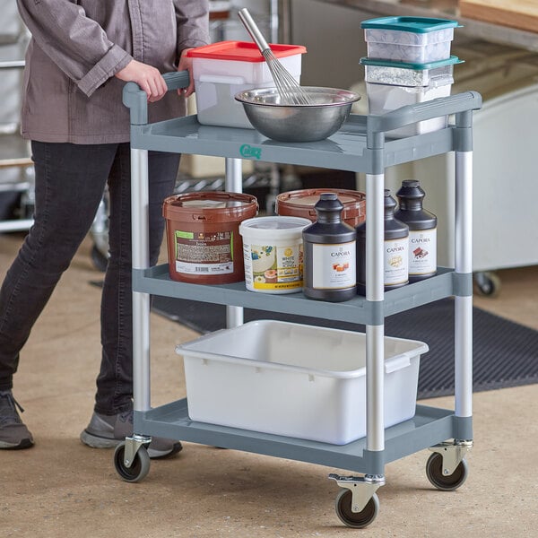 A woman using a gray Choice utility cart with containers on it.