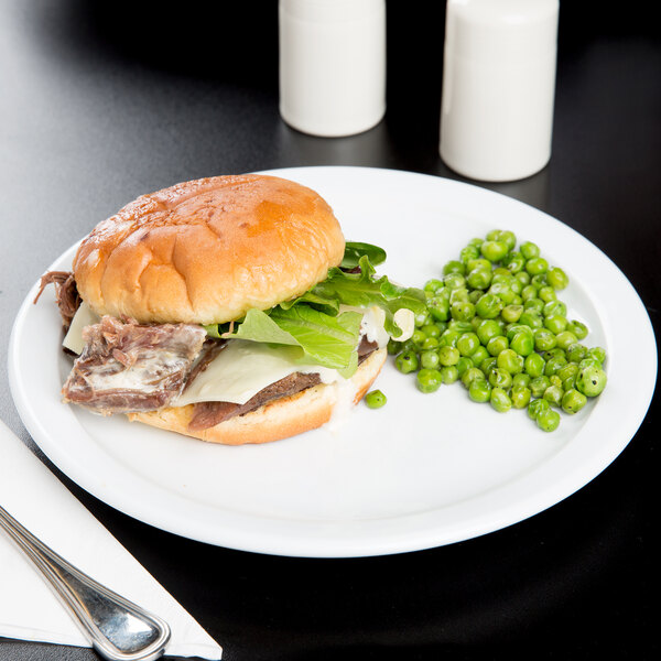 A Cambro white ceramic plate with a sandwich and peas on it.