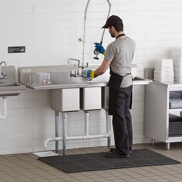 A man in a professional kitchen standing at a Regency 3 compartment sink.