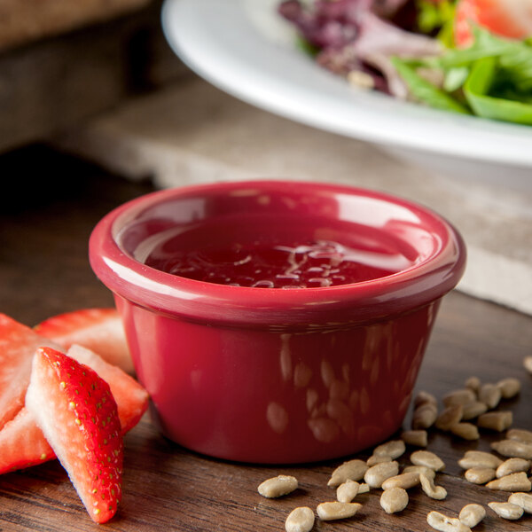 A Carlisle red smooth melamine ramekin filled with fruit and sauce on a table next to a salad.