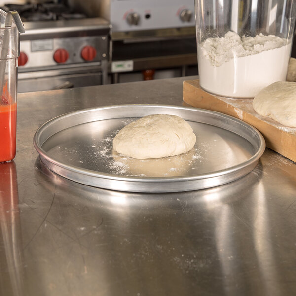 A ball of pizza dough being placed on an American Metalcraft aluminum pizza pan on a counter.