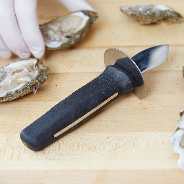 A Victorinox Frenchman style oyster knife on a wooden cutting board with oysters.