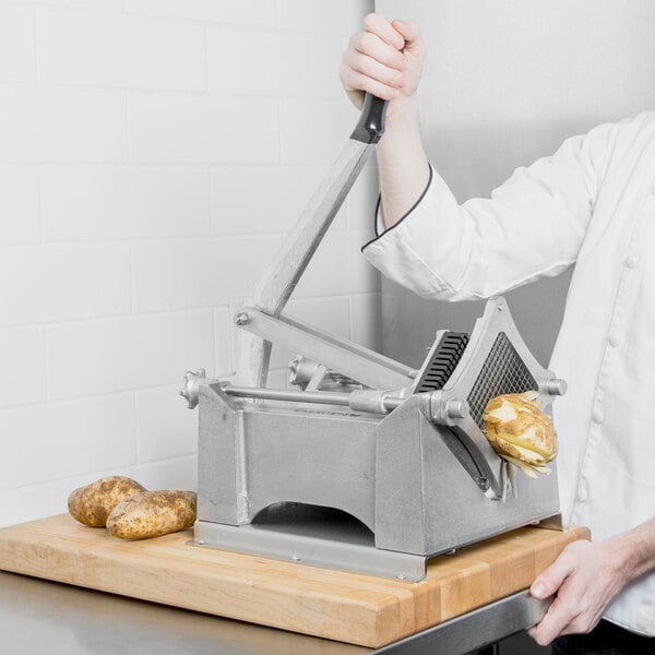 A person in a white chef's coat using a Nemco Monster FryKutter to cut potatoes.