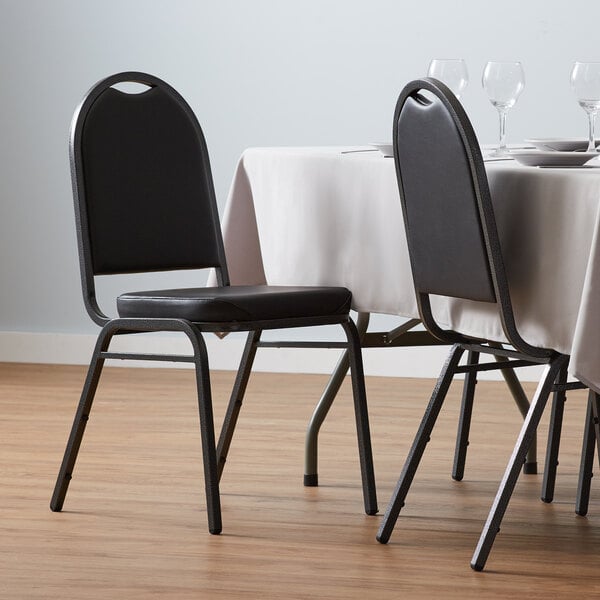 A black Lancaster Table & Seating banquet chair with a padded seat and silver vein frame next to a table with a white tablecloth.