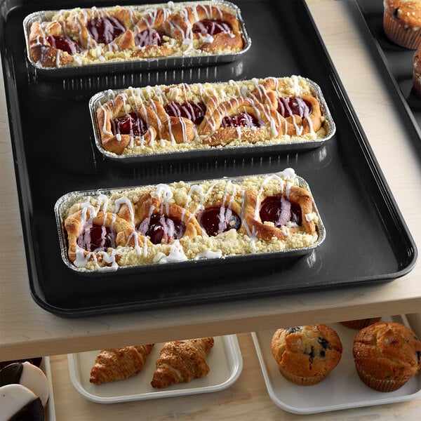 A black Cambro market tray on a counter with pastries and muffins.