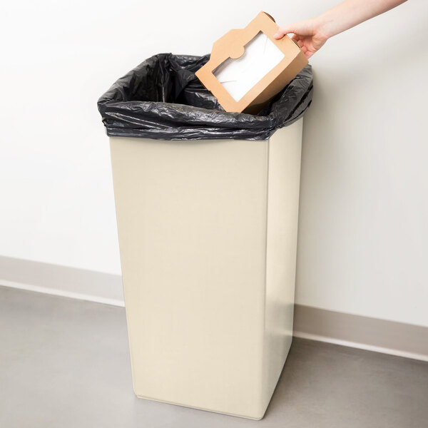 A hand putting a cardboard box into a beige Continental Swingline trash can.