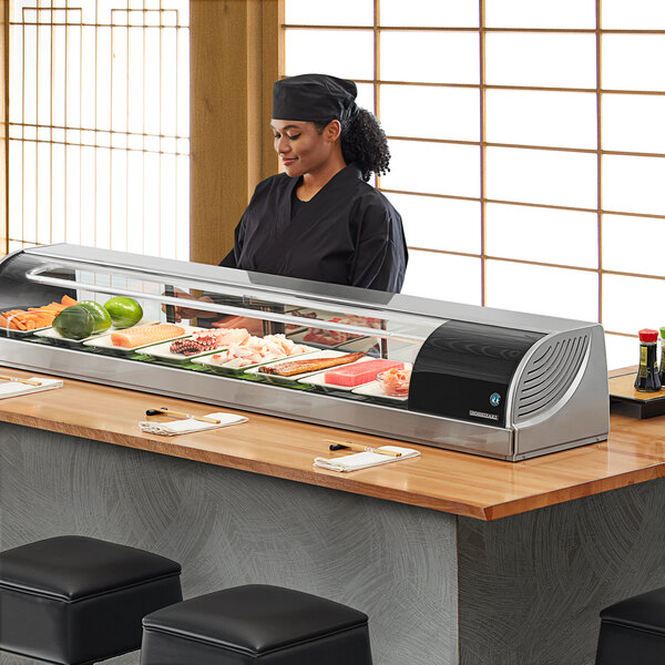 A Hoshizaki refrigerated sushi display case on a counter in a sushi bar with a woman serving sushi.