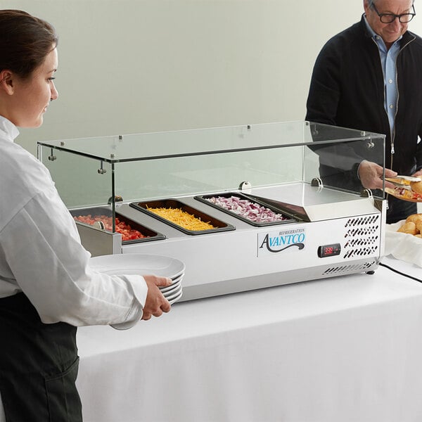 A woman serving food at a hotel buffet using an Avantco clear acrylic sneeze guard.