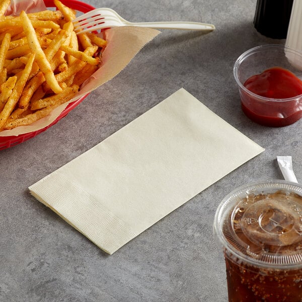 A basket of french fries next to a Choice ecru 2-ply paper napkin and a drink.