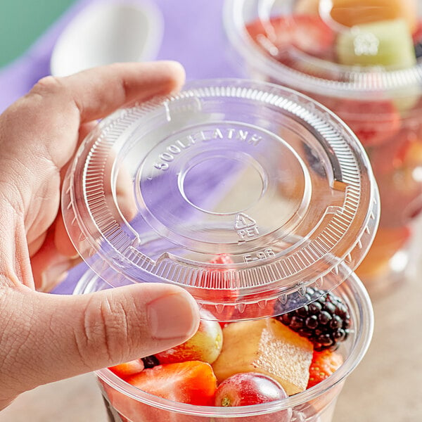 A hand holding a clear plastic container of red and orange fruit with a Choice clear plastic lid on it.