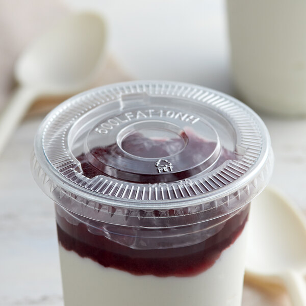 A plastic container with red and white dessert and a clear plastic lid with no straw slot containing red jelly.