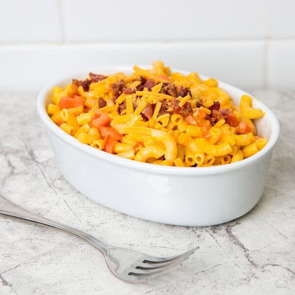 A white oval porcelain serving platter with macaroni and cheese and bacon on a table.