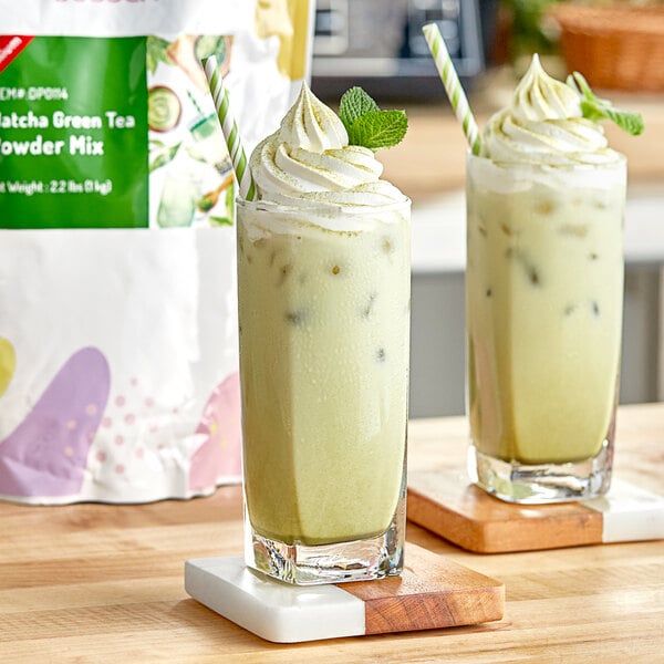Two glasses of green matcha tea with whipped cream and mint leaves.