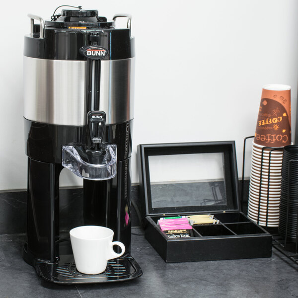 A Bunn stainless steel coffee server on a black base with a white mug on it.