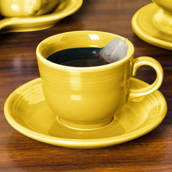 A yellow Fiesta saucer with a tea cup on it and a tea bag.