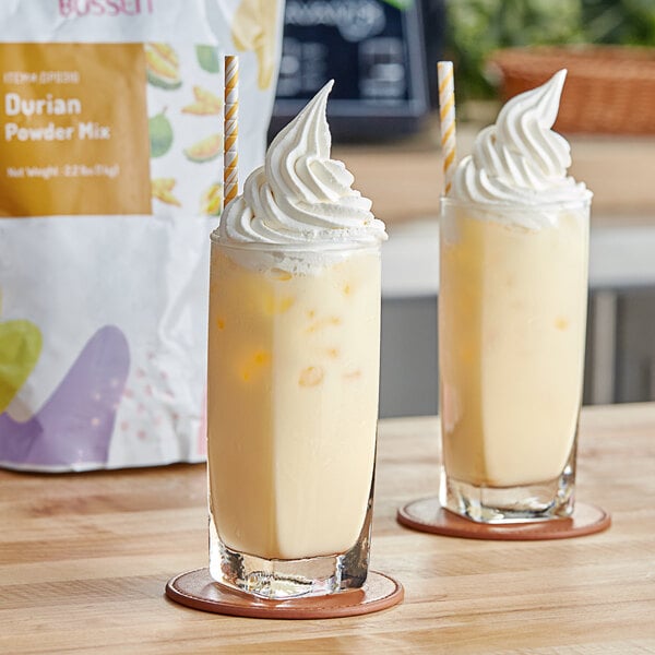 A close up of two glasses of durian milkshake with whipped cream on top.