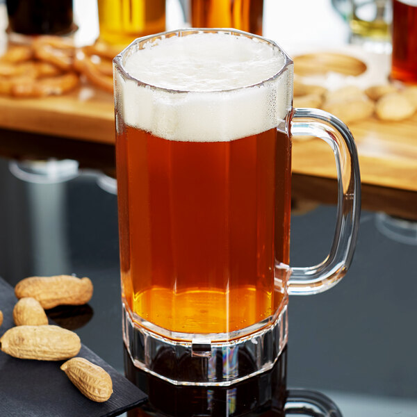 A clear plastic beer mug filled with beer on a table with peanuts.