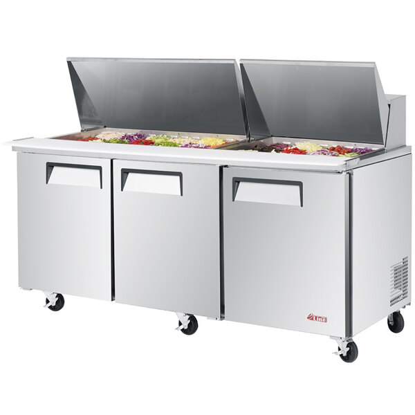 A Turbo Air stainless steel 3 door refrigerated salad prep table with trays of food inside.