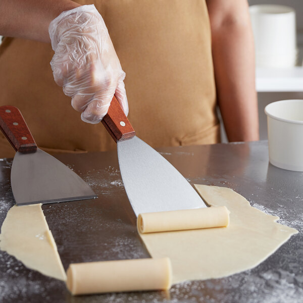 A person using a Tablecraft Rolled Ice Cream Scraper to cut ice cream on a counter.