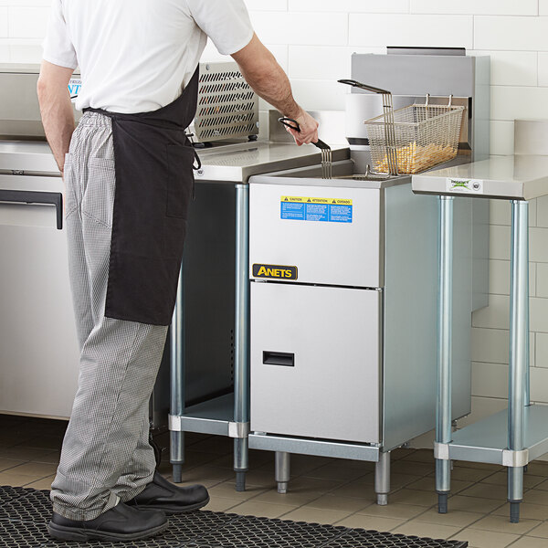 A man in a white shirt and apron using an Anets liquid propane tube fired fryer on a counter in a commercial kitchen.