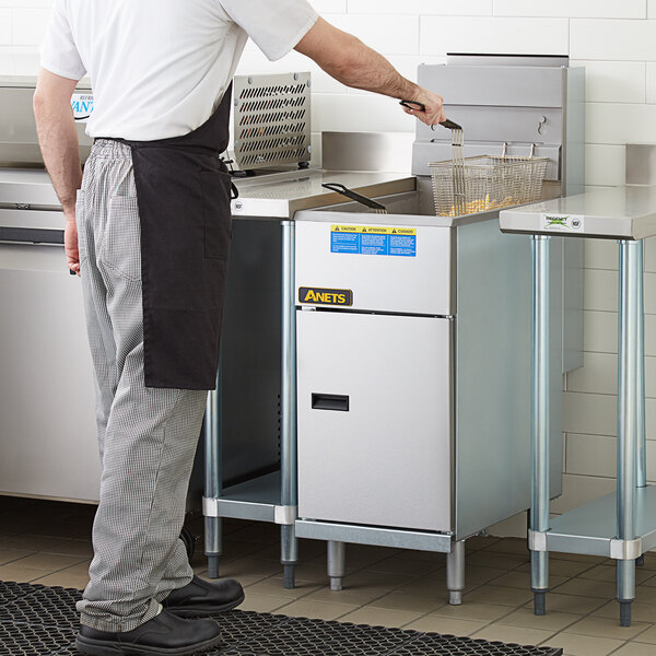 A man in a white shirt and apron using an Anets liquid propane tube fired fryer in a commercial kitchen.