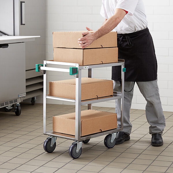 A man pushing a Regency stainless steel utility cart with boxes on the shelves.