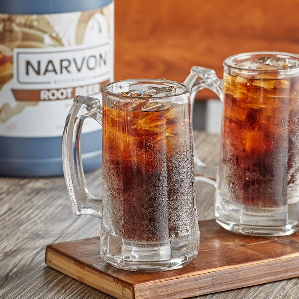 Two glass mugs of Narvon Old Fashioned Root Beer with ice on a wooden surface.