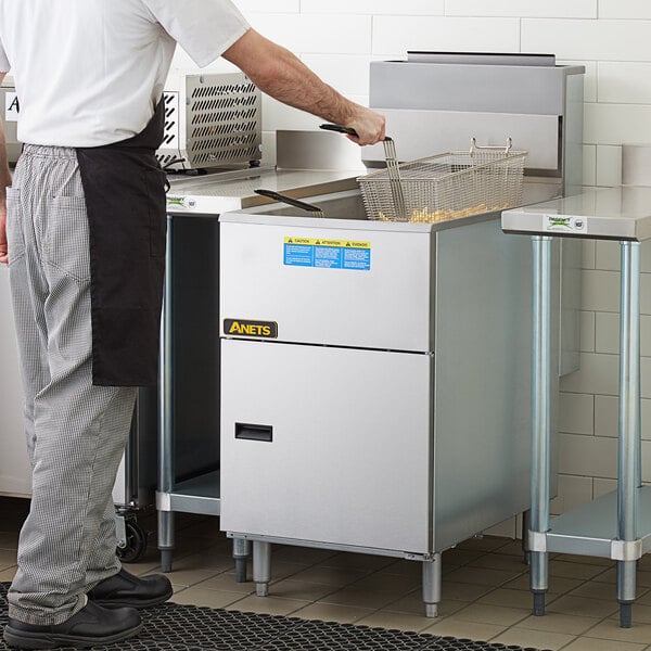 A man standing next to an Anets silver natural gas tube fired fryer on a counter.
