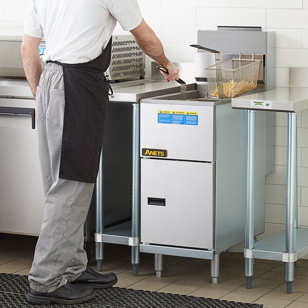 A man in a white shirt and apron standing by an Anets natural gas tube fired fryer.