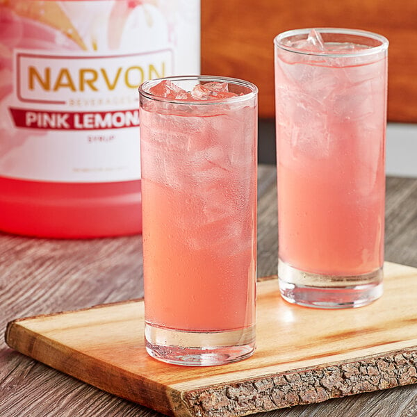 A couple of glasses of Narvon Pink Lemonade with ice on a wooden surface.