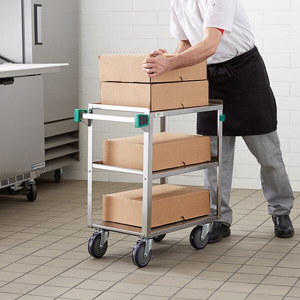 A man pushing a Regency stainless steel utility cart with boxes on it.