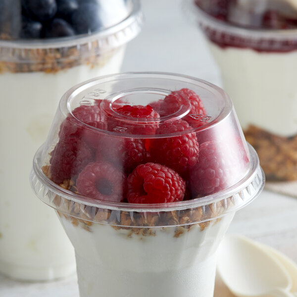A plastic parfait cup filled with yogurt, raspberries, and granola with a clear plastic dome lid.