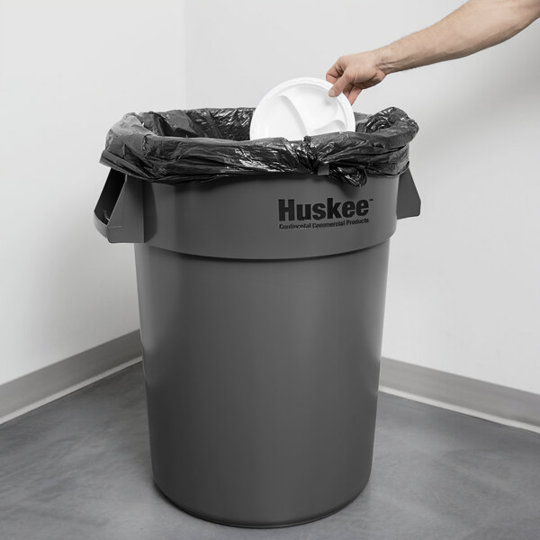 A person placing a plastic lid on a grey Continental Huskee trash can.