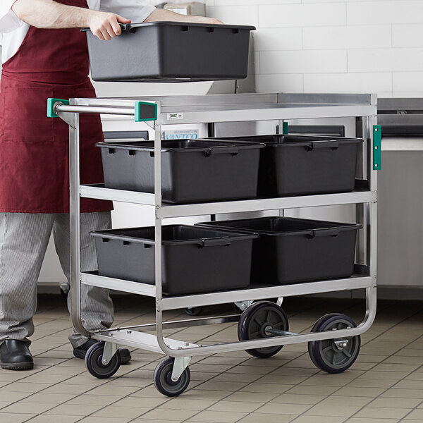 A man standing in a kitchen next to a Regency stainless steel cart with black containers on white shelves.