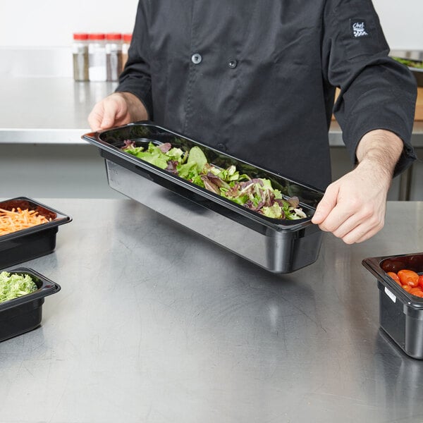 A chef preparing salad in a Cambro black polycarbonate food pan on a counter.