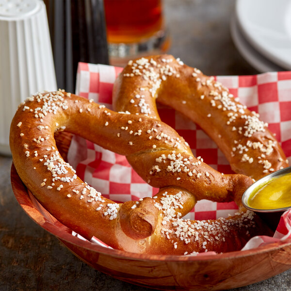 A SuperPretzel King Size soft pretzel with salt on it in a bowl with mustard.