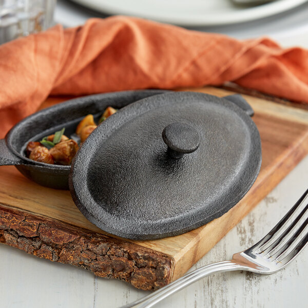 A Vollrath pre-seasoned mini cast iron oval cover on a cast iron pan with a fork.