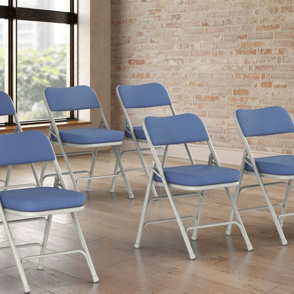 A row of blue Lancaster Table & Seating folding chairs with blue cushions.