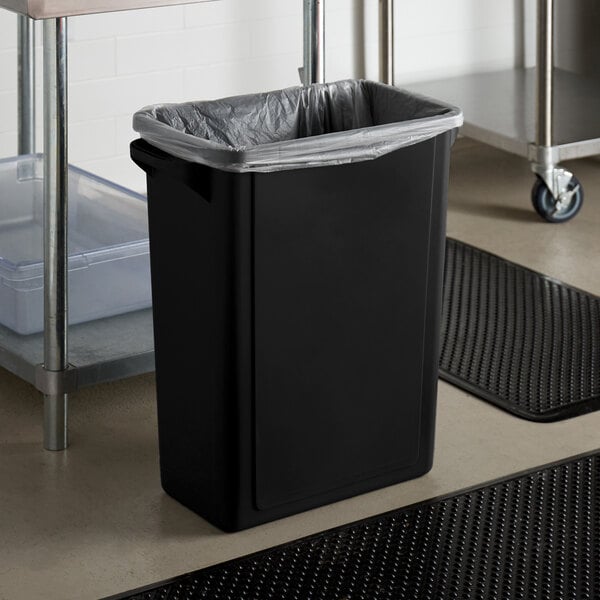 A Lavex black rectangular trash can on a kitchen floor with a plastic bag inside.