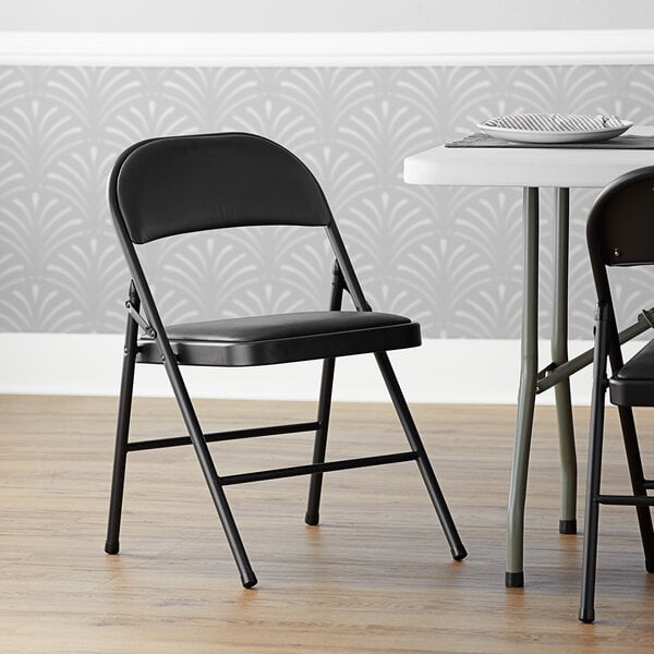 A pair of Lancaster Table & Seating black folding chairs with padded seats next to a table.