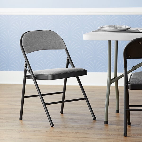 A Lancaster Table & Seating dark grey fabric folding chair with a padded seat in a room.